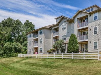 an apartment building with a white fence in front of it  at Residences at Westborough Station, Massachusetts, 01581